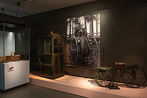 Transportmittel: Sänfte und Laufrad, dahinter ein Foto eines zweisitzigen Hoch-Dreirads. © Histor. Museum Basel.